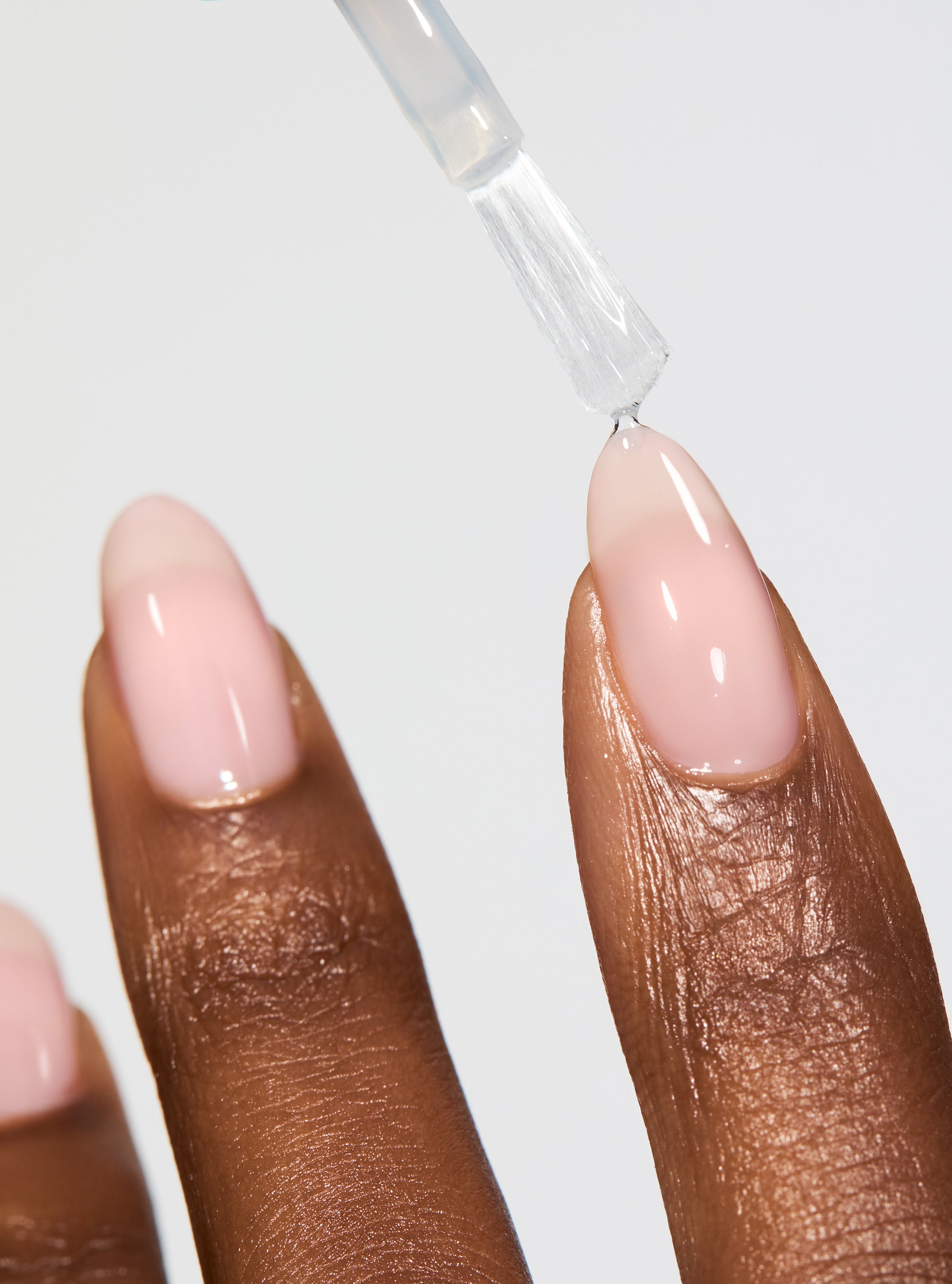 Nail polish being applied to a beige nail with a clear background