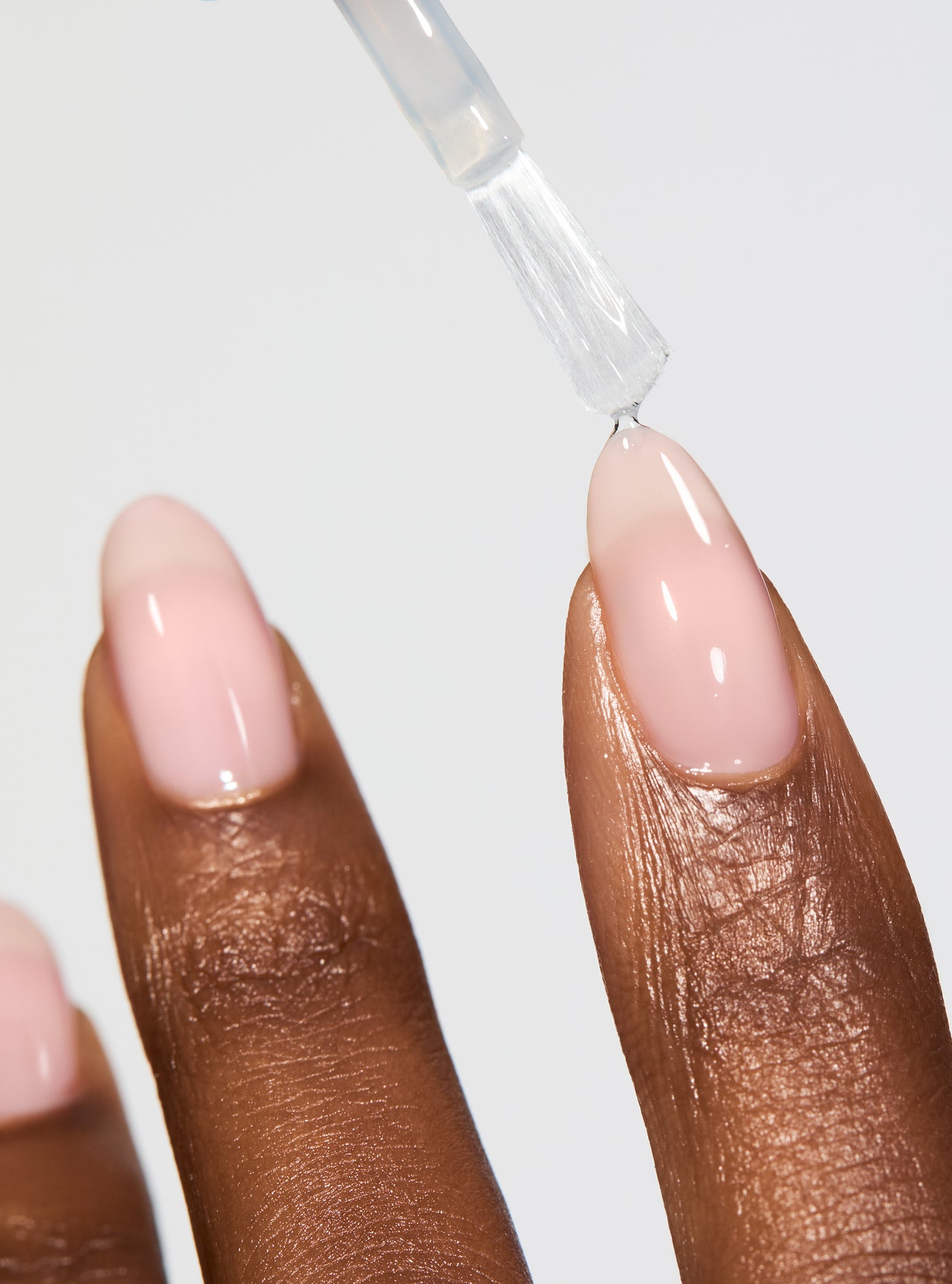 Nail polish being applied to a beige nail with a clear background