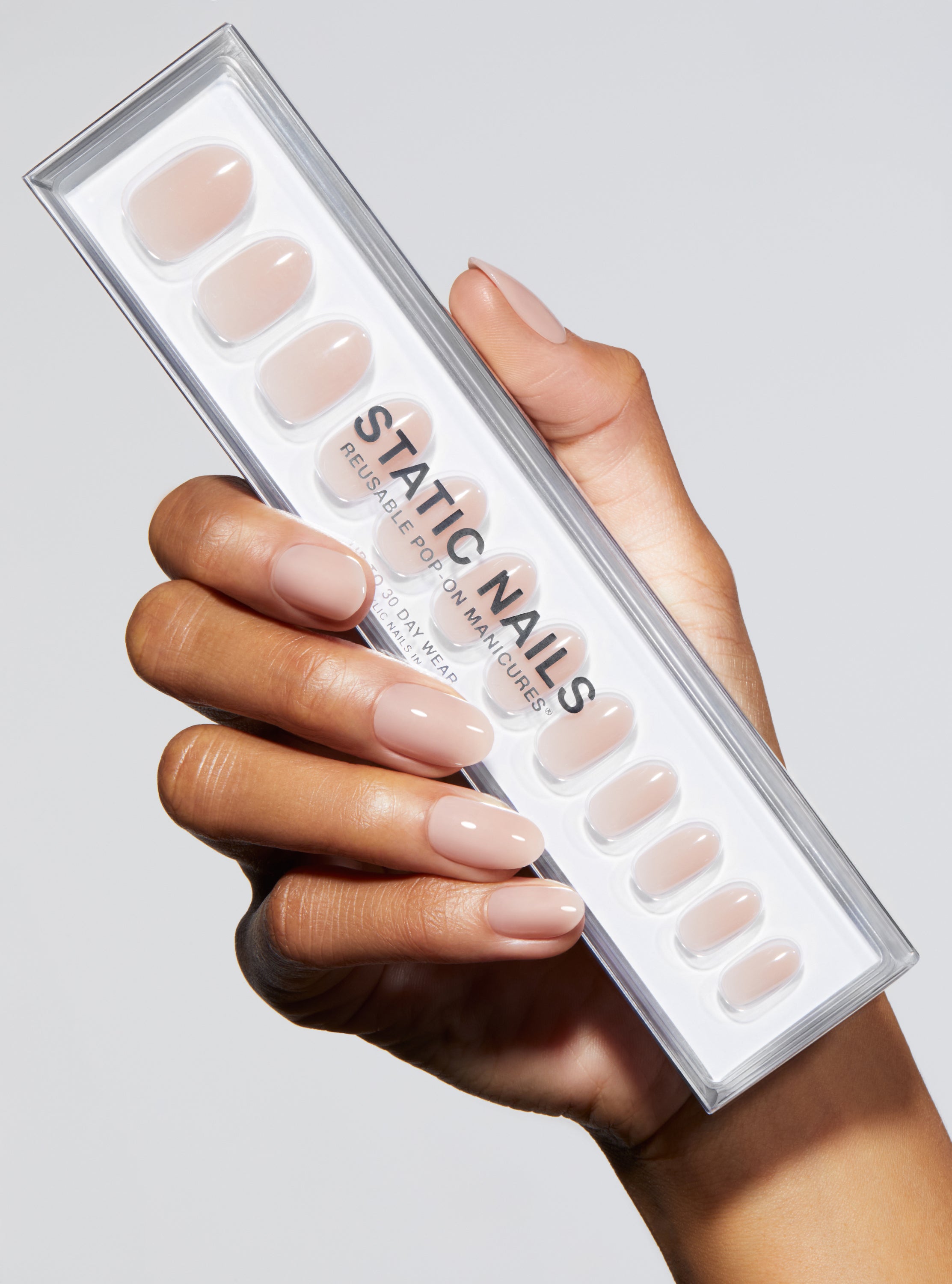 Hand with nude-colored press-on nail on a light gray background