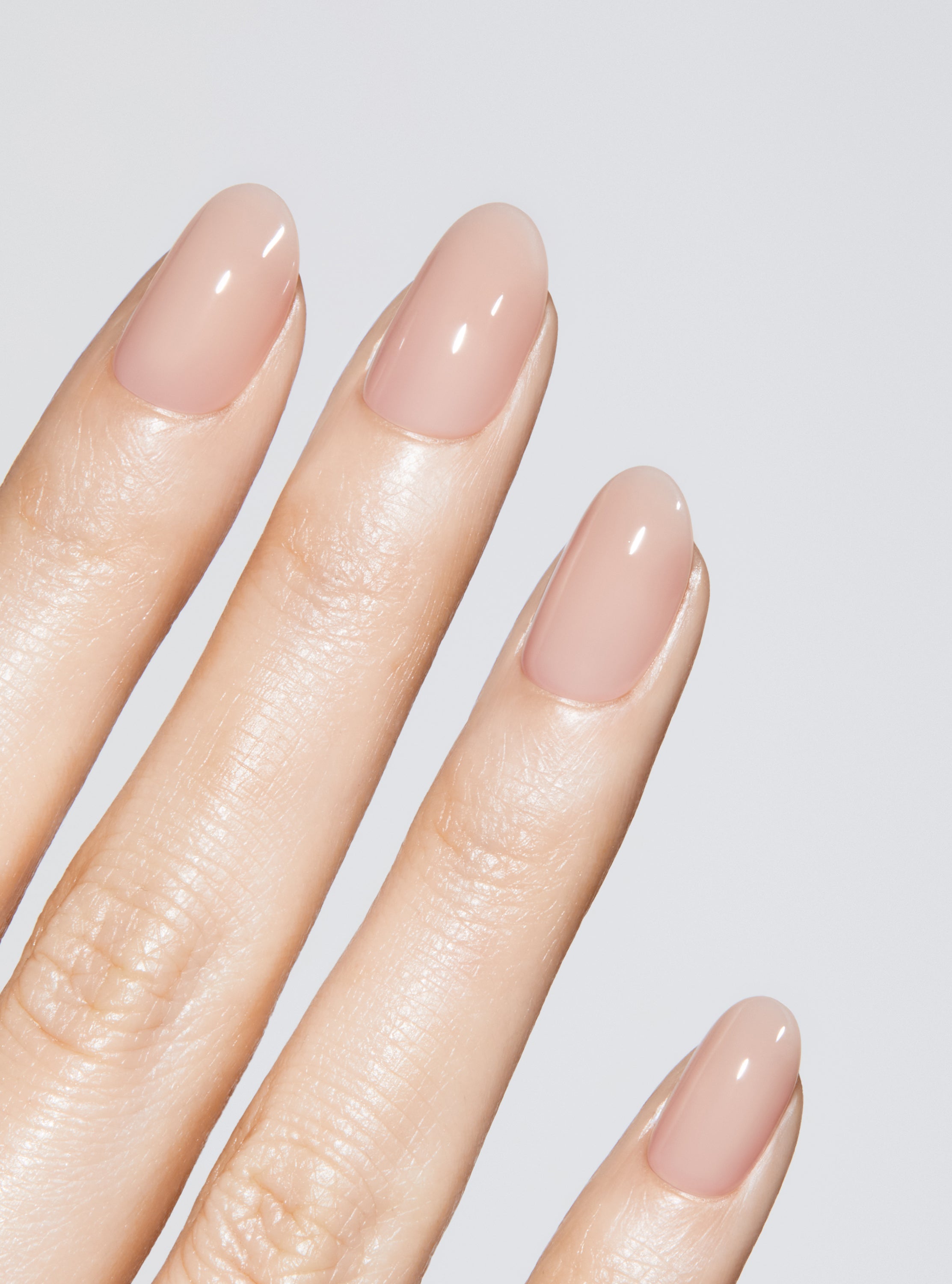 Hand with nude-colored press-on nail on a light gray background