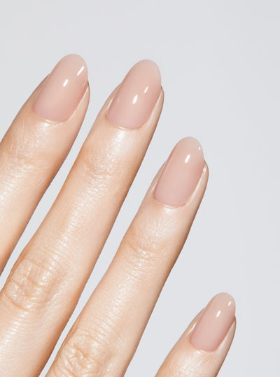 Hand with nude-colored press-on nail on a light gray background