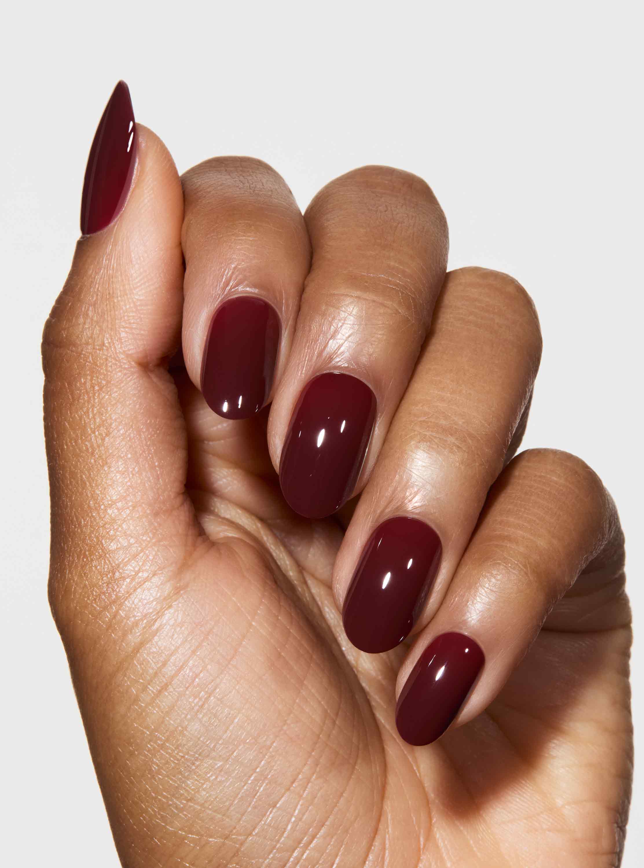 Hand with dark red nail polish on a light background
