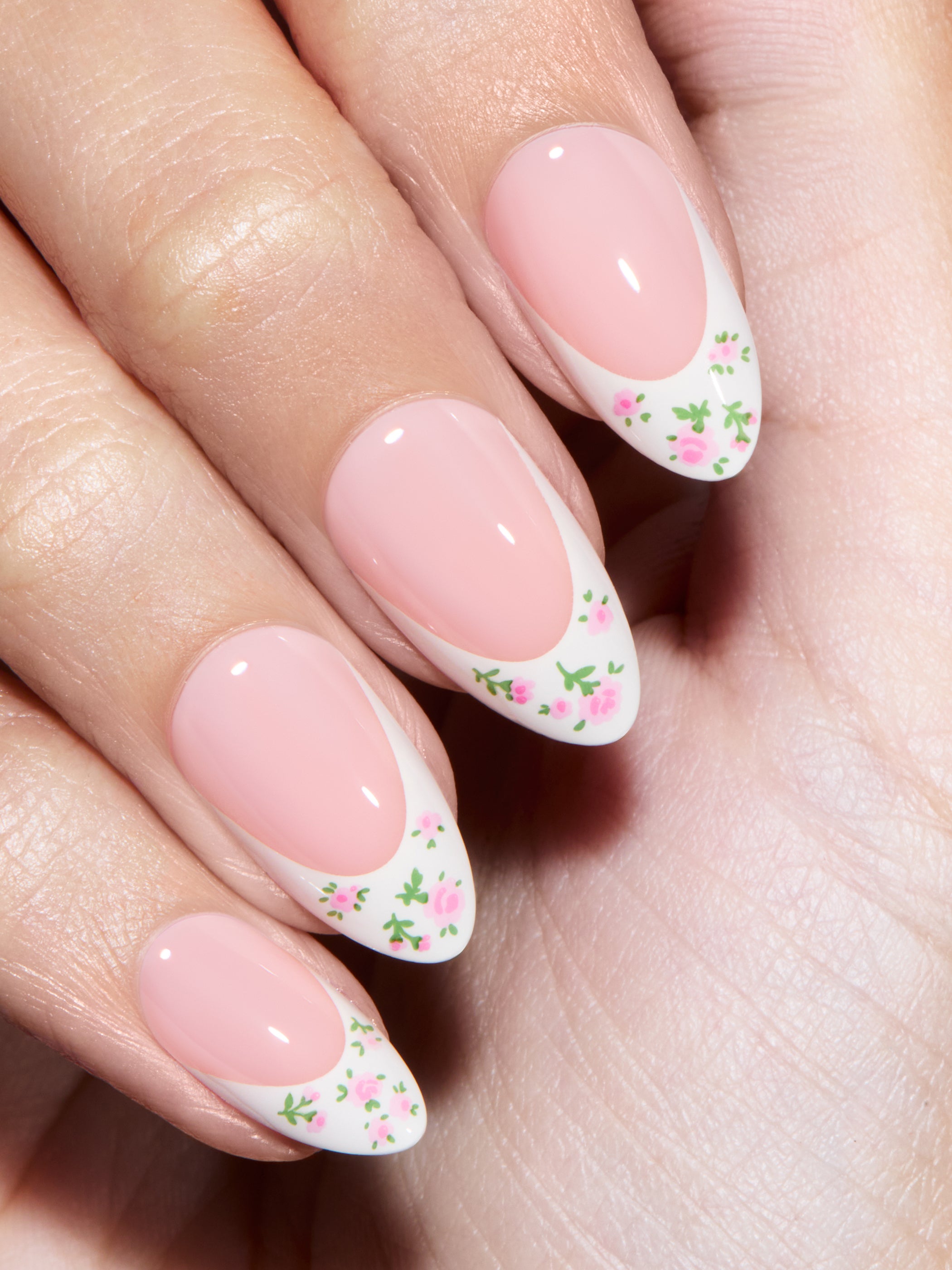 Close-up of a hand with pink nails featuring floral designs on a light background
