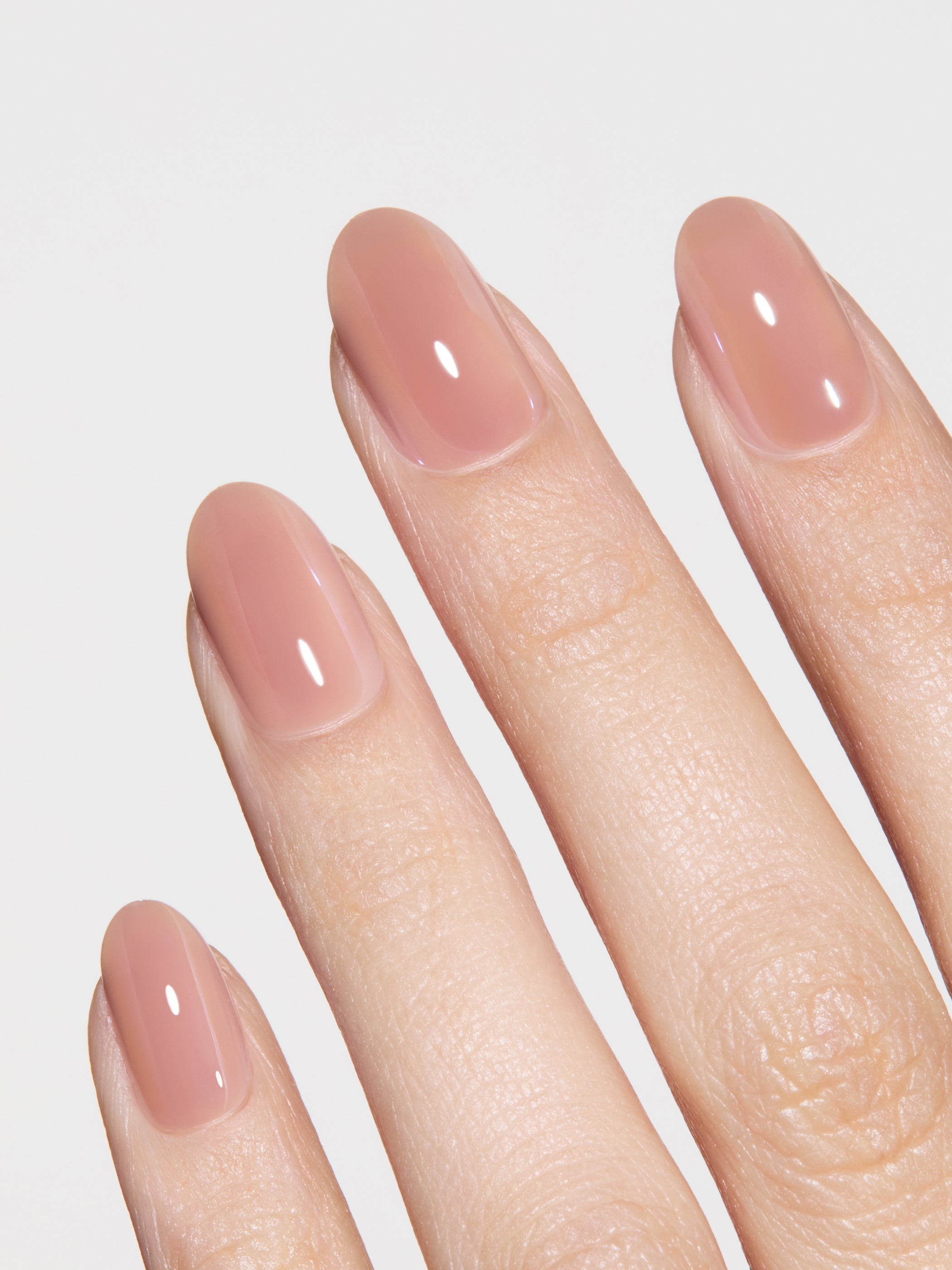 Close-up of a hand with nude-colored nail polish on a light gray background