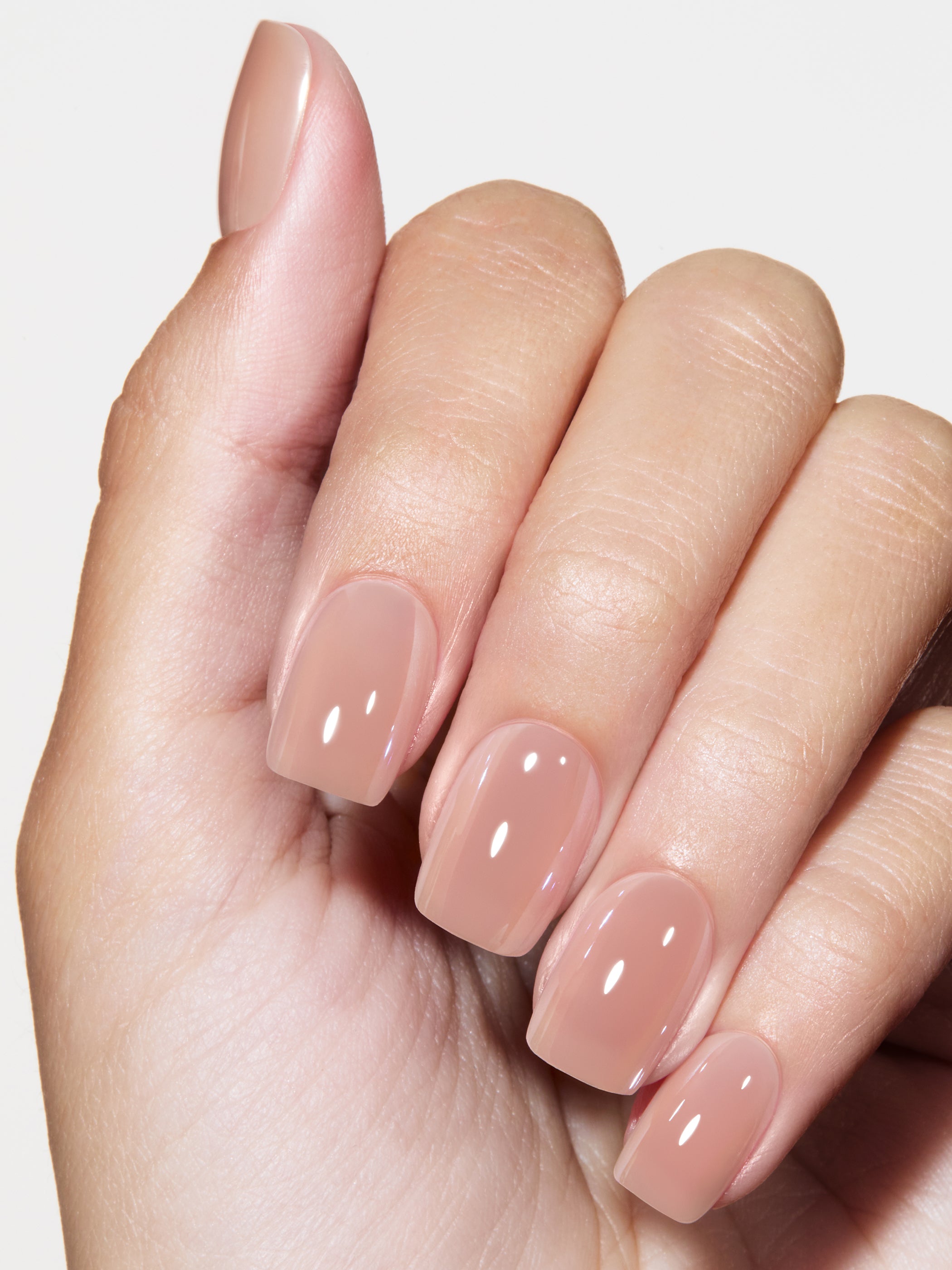 Hand with nude-colored nail polish on a light background