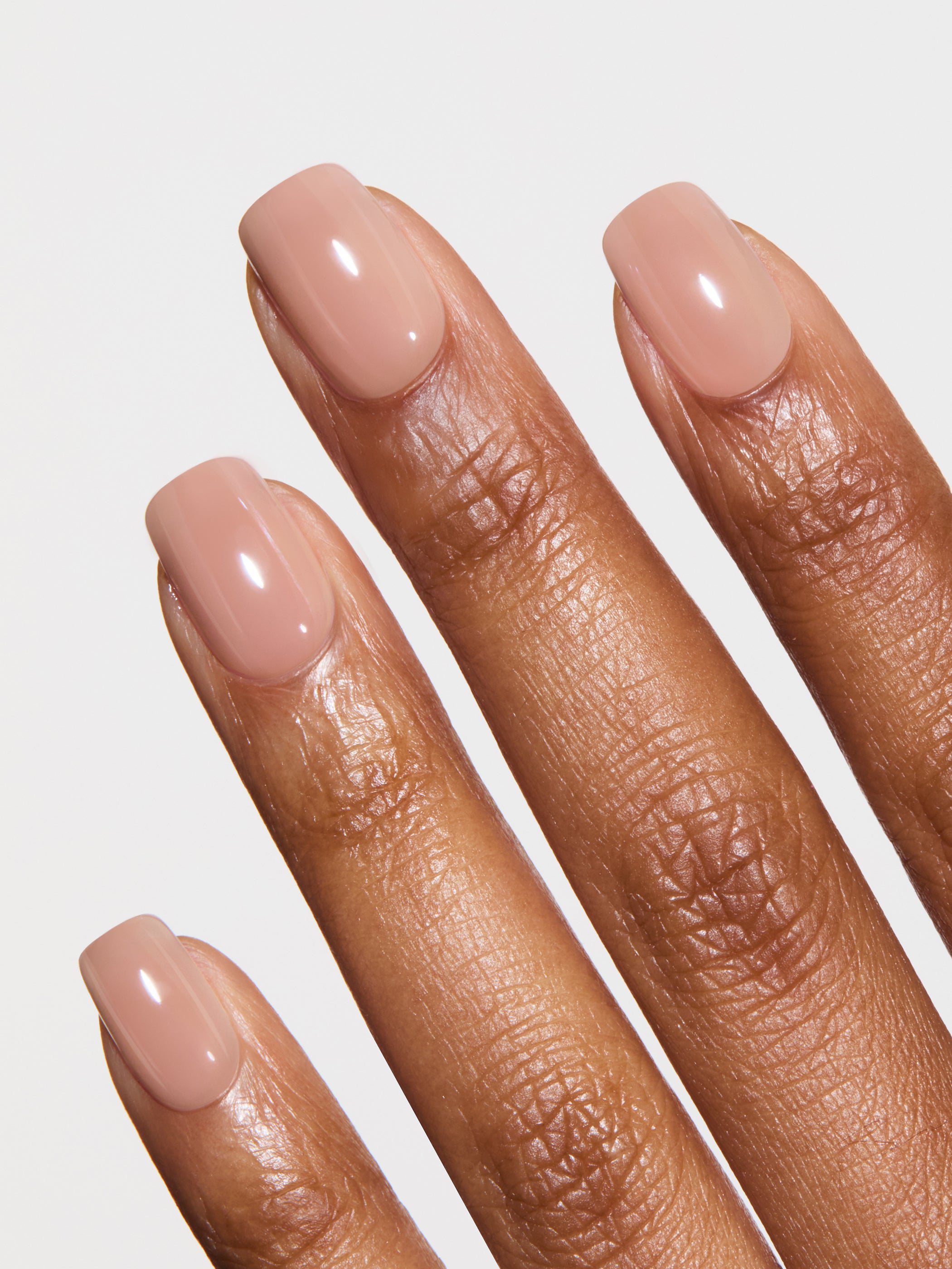 Close-up of a hand with nude-colored nail polish on a light gray background