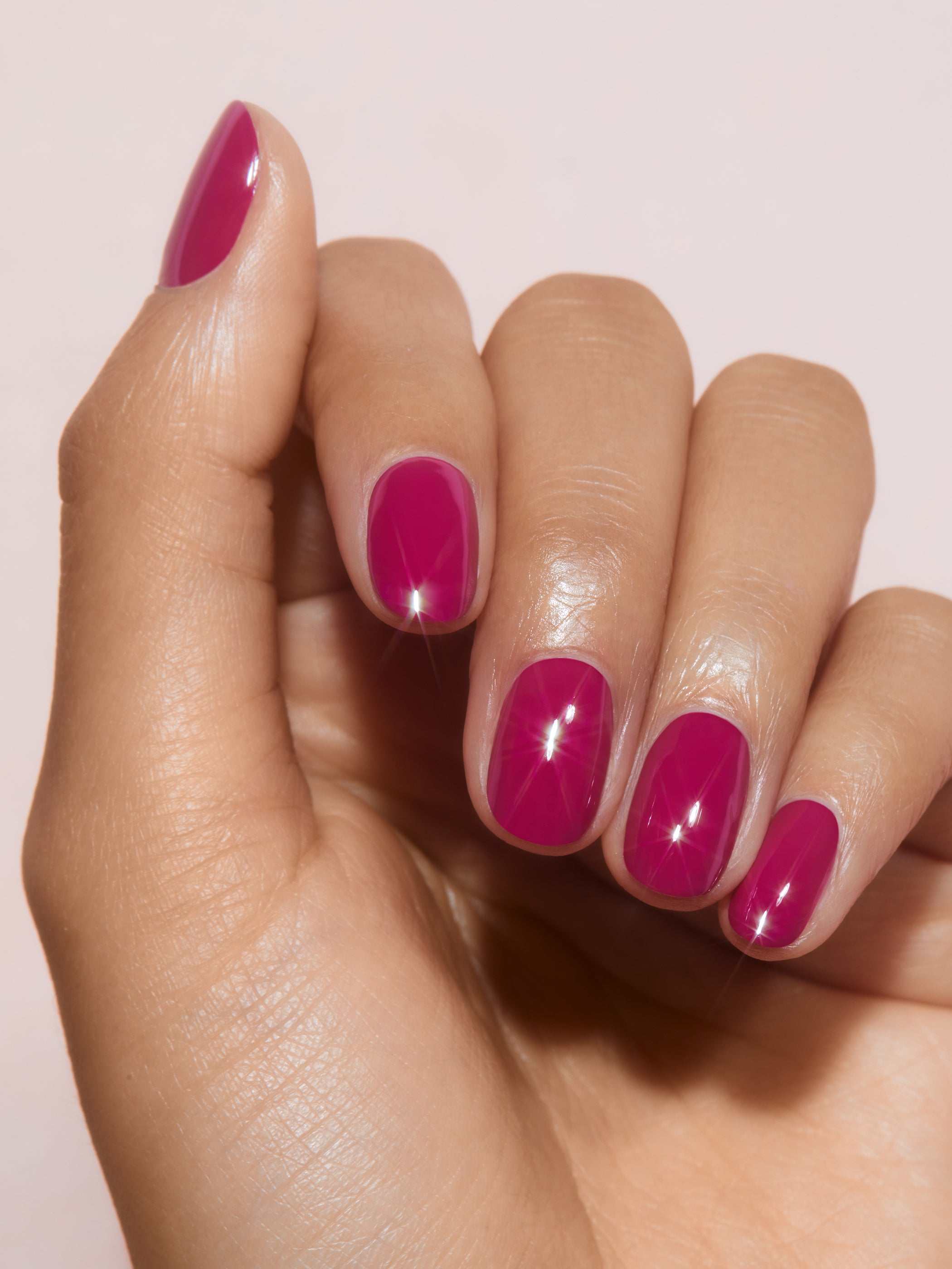 Hand with bright pink nail polish on a light pink background